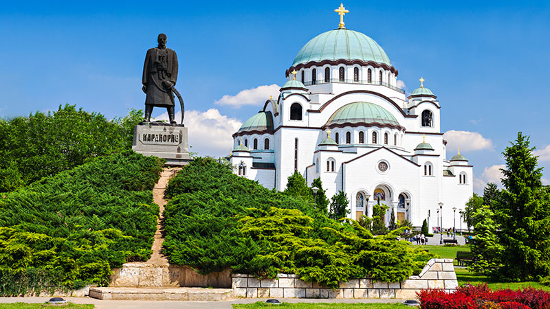 En gammel kirke i byen Beograd med en stor statue ved siden av. Frodig park.