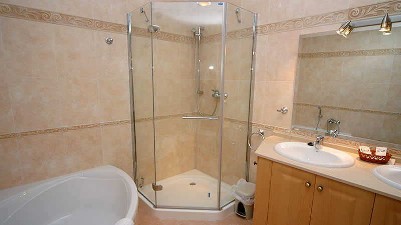 Et baderom med separat badekar og dusj. Vask, skap og speil.