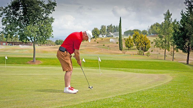 Man i rd skjorte trener p golfputting i Marbella.